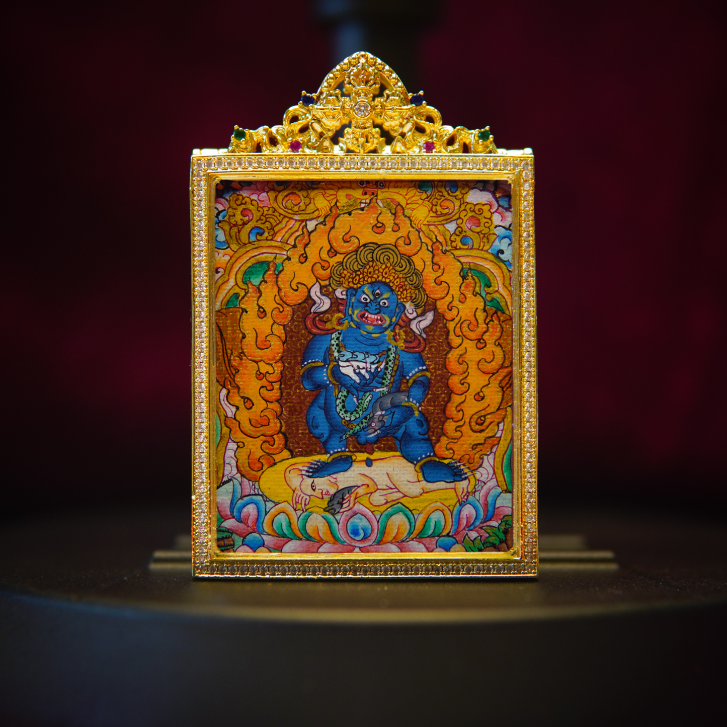 Black Jambhala Tibetan Thangka pendant in ornate gold frame, depicting wealth deity with intricate details and vibrant colors.