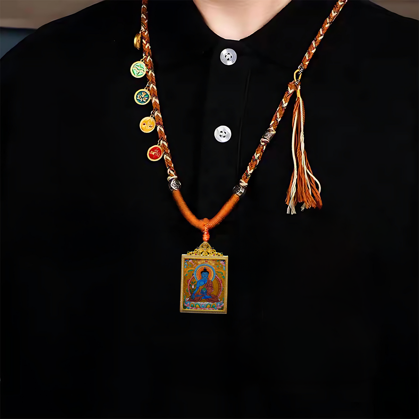 Medicine Buddha Healing Thangka pendant on black shirt with braided cord and charm accents.