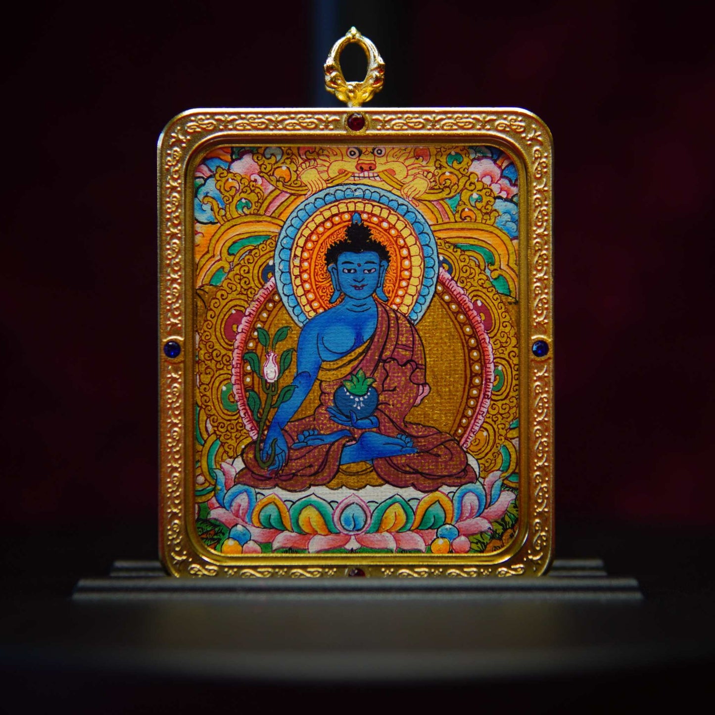 Medicine Buddha Healing Thangka pendant with intricate gold border, featuring celestial blue Bhaisajyaguru on lotus, holding a myrobalan plant and bowl.