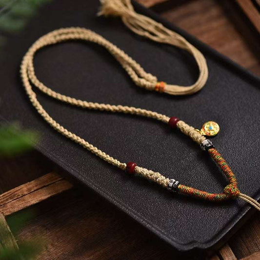 Handwoven Thangka Lanyard with colorful threads and golden accents on black background.