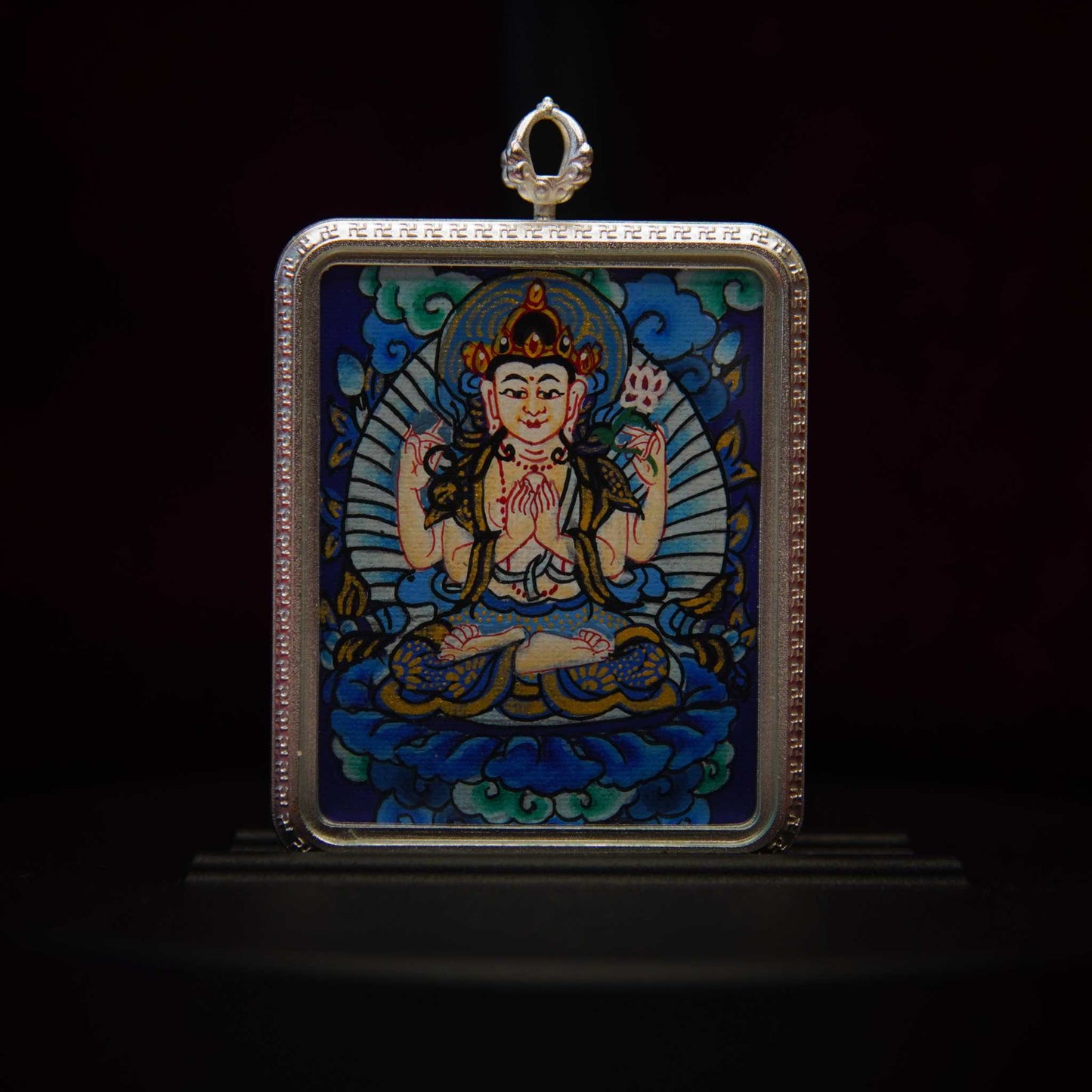 Four-Armed Avalokiteshvara Pendant Necklace depicting the Bodhisattva of Infinite Compassion seated on a lotus throne, with vibrant colors and sacred symbols, against a deep blue background.
