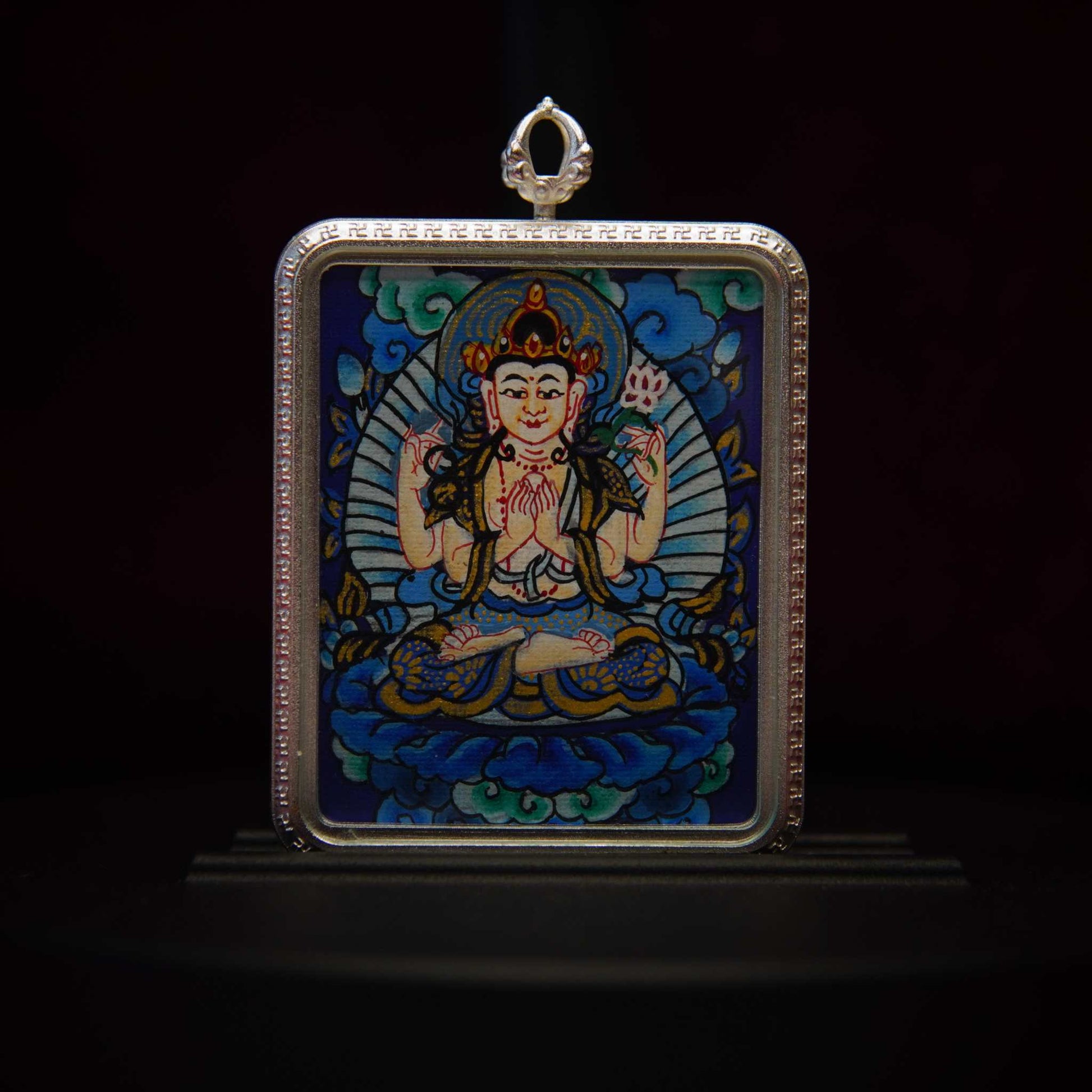 Four-Armed Avalokiteshvara Pendant Necklace depicting the Bodhisattva of Infinite Compassion seated on a lotus throne, with vibrant colors and sacred symbols, against a deep blue background.